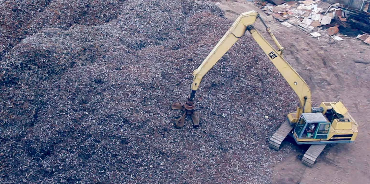 An excavator handling scrap metal in a raw-materials yard